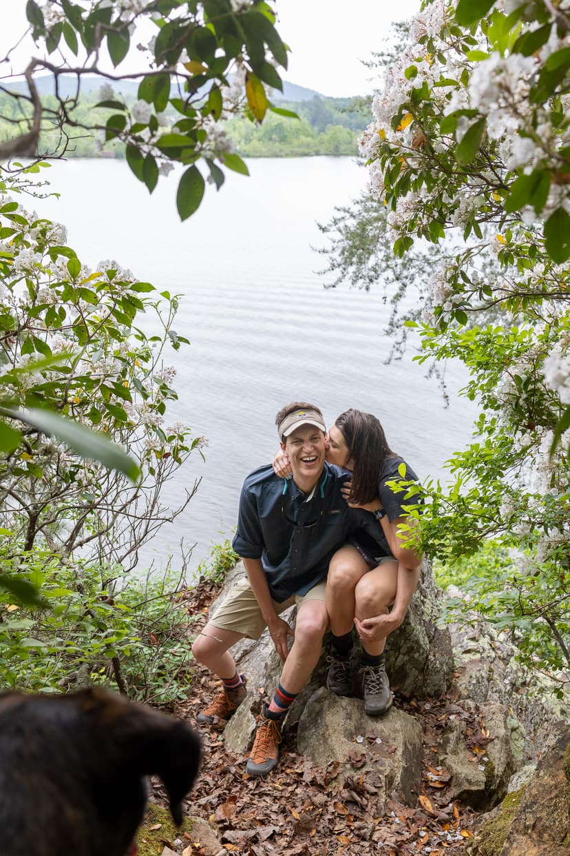 man and woman kissing in front of lake